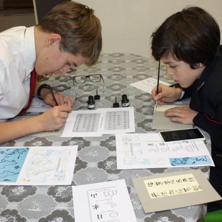 Uczestnicy warsztatów kaligrafują litery japońskiego alfabetu.