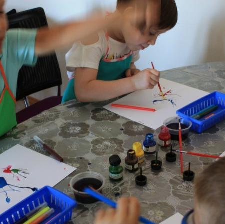 Uczestnicy warsztatów Pałacowa menażeria w sali edukacyjnej tworzą zwierzaki-cudaki za pomocą kolorowego tuszu i flamastrów.