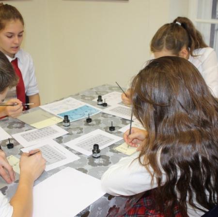 Uczestnicy warsztatów kaligrafują litery japońskiego alfabetu.