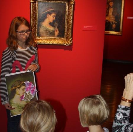 Dziewczynka prezentuje swoją pracę pod obrazem "Dama z wachlarzem" Maurycego Gottlieba.