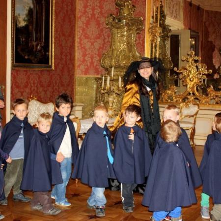 Salon lustrzany. Uczestnicy ubrani w pelerynki. Prowadząca warsztat w stroju z epoki.