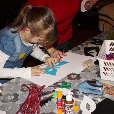 Dziewczynka wykonuje swoją własną maskę za pomocą przygotowanych materiałów na sali balowej w Pałacu Herbsta.