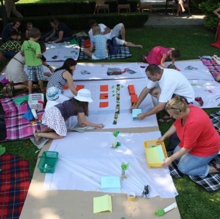 Uczestnicy warsztatów wykonują plan Księżego Młyna na płótnie rozłożonym w przypałacowym ogrodzie - widok z góry.