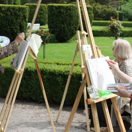 Warsztaty plenerowe w ogrodzie - uczestnicy przy sztalugach.