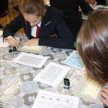 Uczestnicy warsztatów kaligrafują litery japońskiego alfabetu.