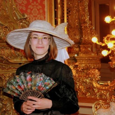 Zdjęcie przedstawia młodą kobietę w kapeluszu i z wachlarzem w dłoni. Kobieta patrzy na nas.