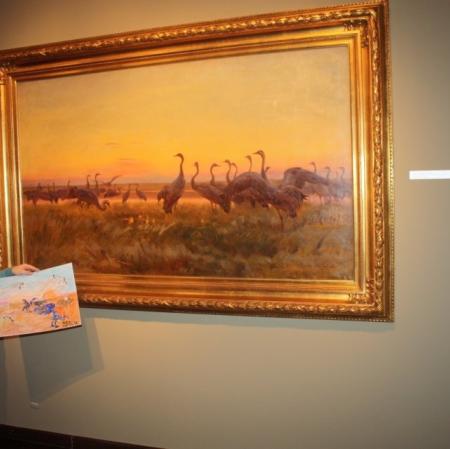 Uczestnik warsztatu prezentuje swoją pracę pod obrazem "Żurawie"  Józefa Chełmońskiego.