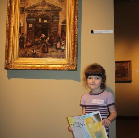 Uczestniczka warsztatu prezentuje swoją pracę pod obrazem "Brama na starym mieście" Aleksandra Gierymskiego.