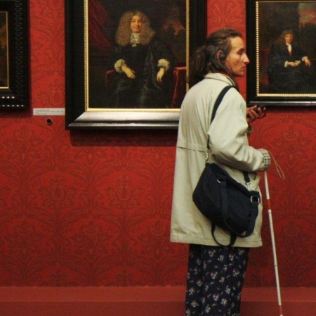 Kobieta z laską stoi przed obrazami  