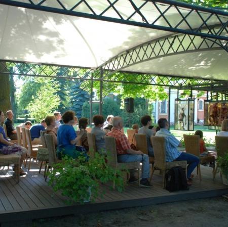 Zapatrzeni widzowie teatralnego przedstawienia "Hamlet" Williama Szekspira w adaptacji Adama Walnego pod altaną Muzeum Pałac Herbsta.