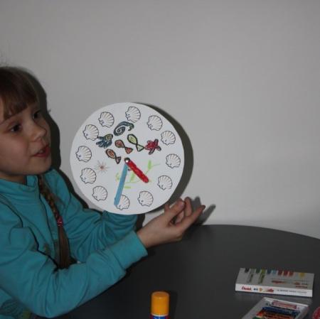 Dziewczynka prezentuje wykonany przez siebie zegar.