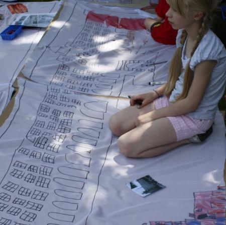 Uczestnicy warsztatów wykonują plan Księżego Młyna na płótnie rozłożonym w przypałacowym ogrodzie.