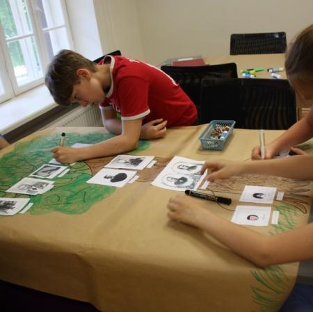 Czworo uczestników warsztatów "Drzewo pokoleń"  wykonuje na szarym papierze drzewo genealogiczne rodziny Herbstów.