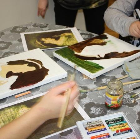 Zbliżenie na dłonie uczestników oraz powstające prace malarskie. Na stole paleta malarska, pędzle, pastele.