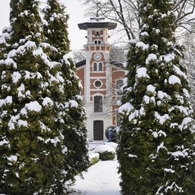 Zdjęcie przedstawia zimowy pejzaż. Na drugim planie wieża budynku z cegły.