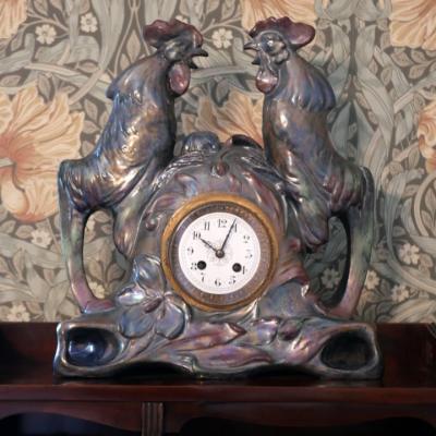 Zegar udekorowany dwoma kogucikami ustawionych na przeciwko siebie.