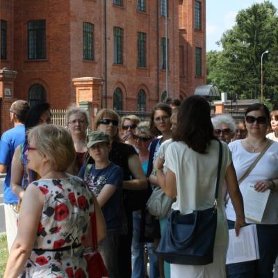Zdjęcie: liczna grupa dorosłych stoi na chodniku przed dawną Nową Przędzalnią Scheiblera.