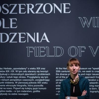 Kobieta stojąca na tle ściany, nad nią napis "Poszerzone pole widzenia"