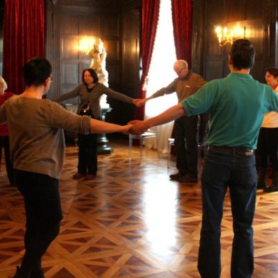 Zdjęcie: kilka osób dorosłych we wnętrzu wielkiej sali trzyma się za ręce w kole.