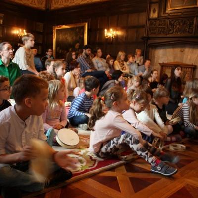 Zdjęcie: Liczna grupa dzieci siedzi na podłodze w dużej sali. Wszyscy patrzą w jednym kirunku.