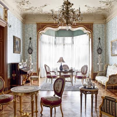 Zdjęcie: wnętrze, w którym stoją liczne krzesła, kanapa i fotel obite wzorzystą tkaniną, stoczki i pianino.