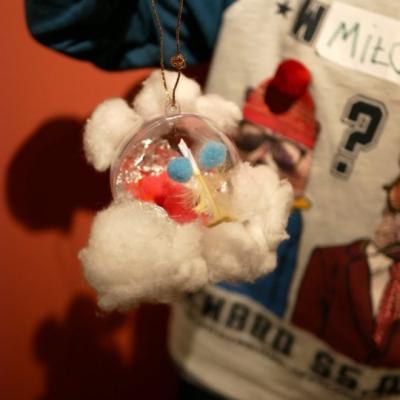 Zbliżenie na własnoręcznie wykonaną ozdobę świąteczną, na przezroczystej bombce przyklejone białe kłębki waty, przypominają brodę św. Mikołaja. 