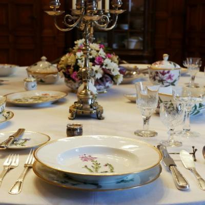 Bogato zstawiony stół z rzędami sztućców, porcelaną, i kryształami. 