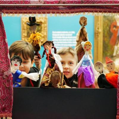 Niewielki teatrzyk z różową kurtyną, za nim dzieci trzymające kukiełki