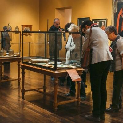 Tłum ludzi w dużej sali, gdzie na ścianach wiszą obrazy, a także stoją gabloty.