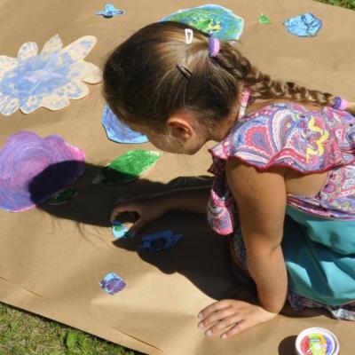 Zdjęcie: dziewczynka kuca nad wielkim arkuszem szarego papieru.