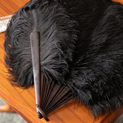 Na stoliku leżą wachlarz z czarnych piór i naszyjnik z koralików