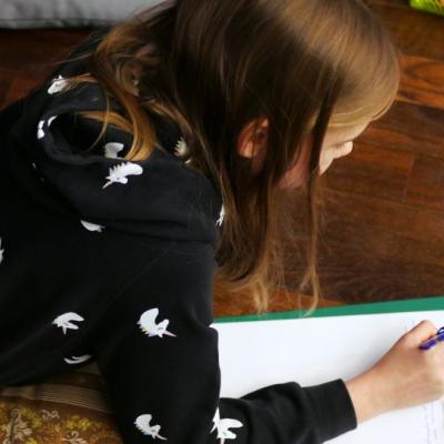 Dziewczynka leżąca na podłodze, pisze na kartce