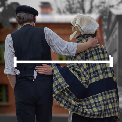 Dwójka ludzi ubrana w stroje z przełomu XIX i XX wieku idzie razem, obejmując się ramionami. Mężczyzna w ciemnej kamizelce i czapce oraz kobieta w chustce i kraciastej narzucie. Przez ich plecy przechodzi pozioma biała linia.