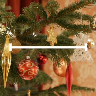 Udekorowana choinka widziana z bliska. Wśród zielonych gałązek wiszą różne ozdoby świąteczne w kolorach złotym i czerwonym, w tym błyszczące bombki, złota soplówka, gwiazdka oraz biały, koronkowy aniołek.