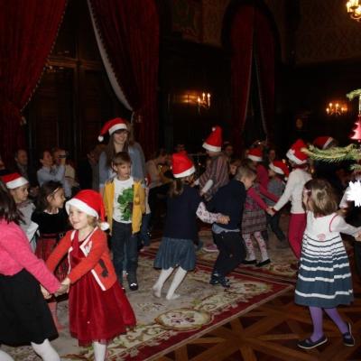 Dzieci w mikołajkowych czapkach ruszają się po dużej sali. Po prawej fragment ozdobionej choinki