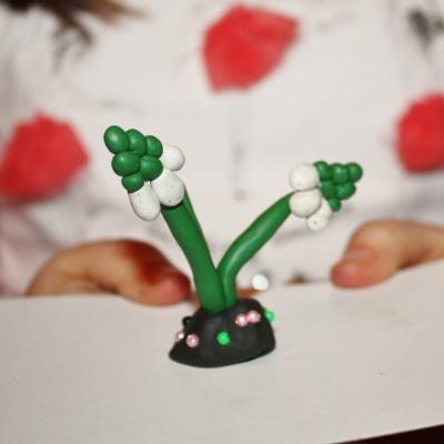 praca z plasteliny przedstawia białe kwiatki na zielonych łodyżkach