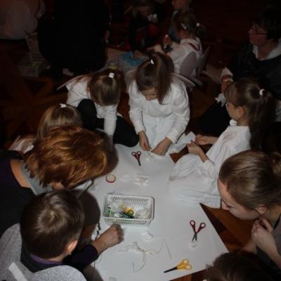 Kilkoro dzieci na podłodze są pochylone nad białym arkuszem. w dłoniach trzymają nożyczki, klej i białe kartki